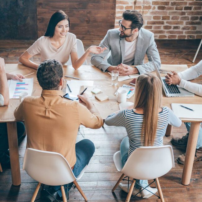 Top view of young business people discussing something while sitting at the office desk together